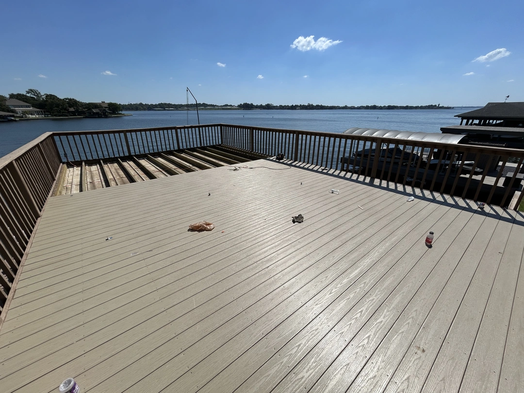 A beige composite deck in the process of being built, overlooking a lake with houses along the far shore.